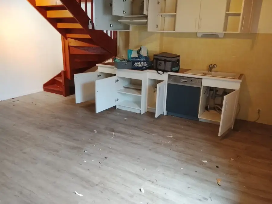 Avant intervention : coin cuisine du séjour, sol jonché de débris et placards vidés portes ouvertes